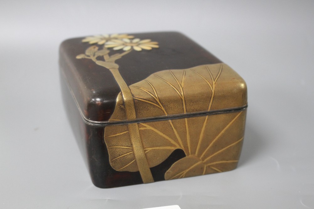 A Japanese Meiji period lacquer box, decorated with lotus leaves and flowers, with the petals inset with mother of pearl, silver rim an